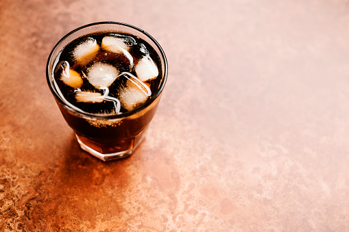 Glass of Iced black coffee against a copper backdrop.