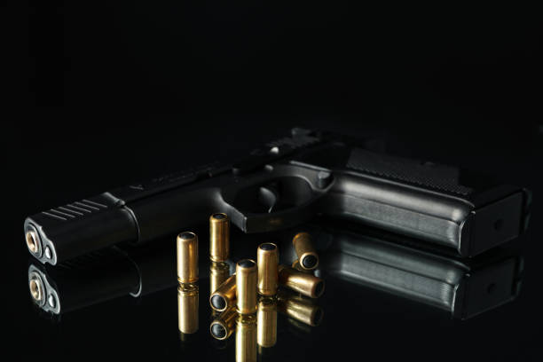 istock Pistol and bullets on mirror table against black background 1253189551