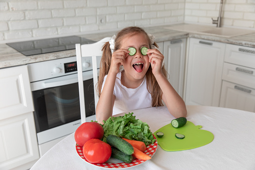little girl in the kitchen closes her eyes with cucumbers. the child in kitchen
