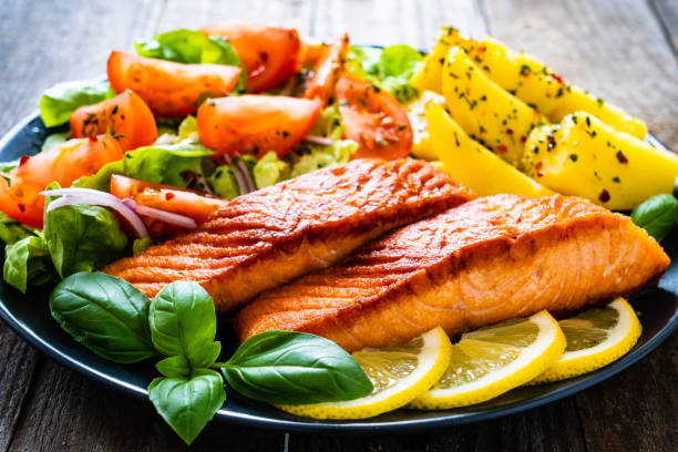istock Fried salmon steak, fried potatoes and vegetables on wooden background 1253199094