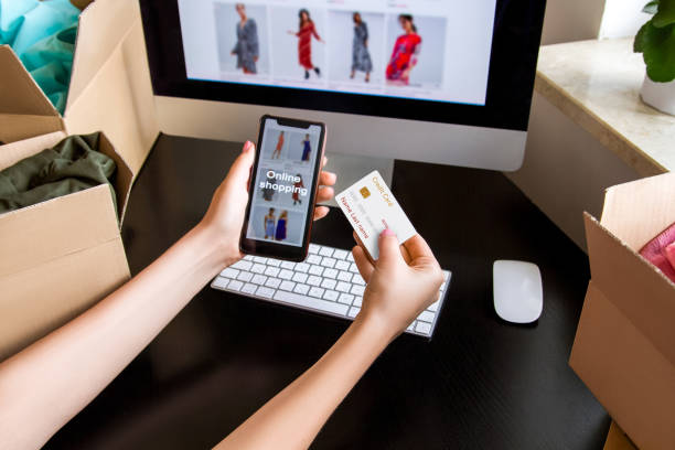 istock Credit card and phone in a hand. Computer screen. boxes, keyboard, mouse.- 1253206377
