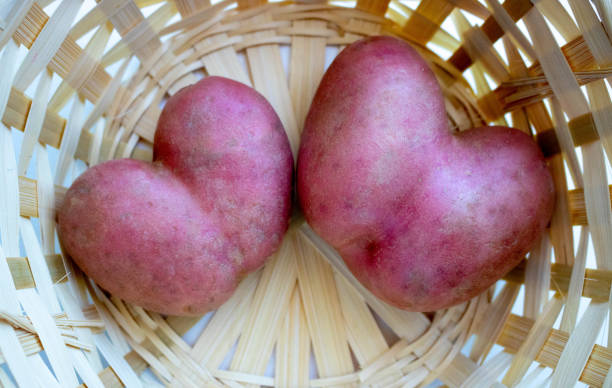 dwa czerwone ziemniaki w kształcie serca są w koszu. zbliżenie ziemniaczanego serca - heart shape raw potato food individuality zdjęcia i obrazy z banku zdjęć