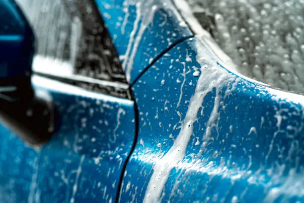 Blue car wash with white soap foam. Auto care business. Car cleaning and shining before waxing service. Vehicle cleaning service with antiseptic and disinfection of coronavirus (COVID-19). Carwash.