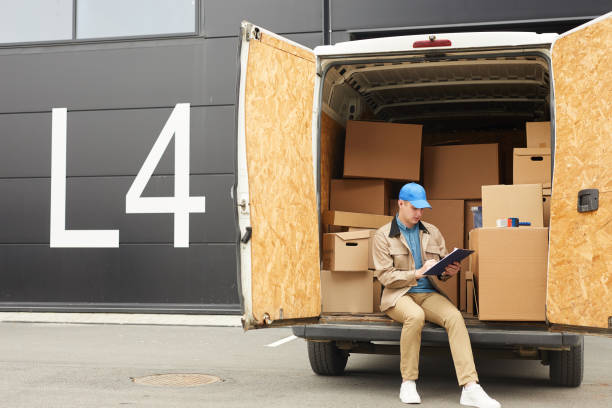 Man working in cargo delivery Young man in uniform filling documents while sitting on the van he working in cargo delivery mover delivery person box hand truck stock pictures, royalty-free photos & images