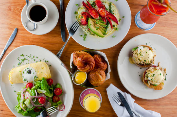 istock Breakfast or brunch table w/ food. Eggs Benedict. Eggs, Lobster, bacon, bagels, rolls, croissants, omelettes garnished w/ parsley & avocado. Classic American, French or Italian restaurant breakfast or brunch. 1253222532