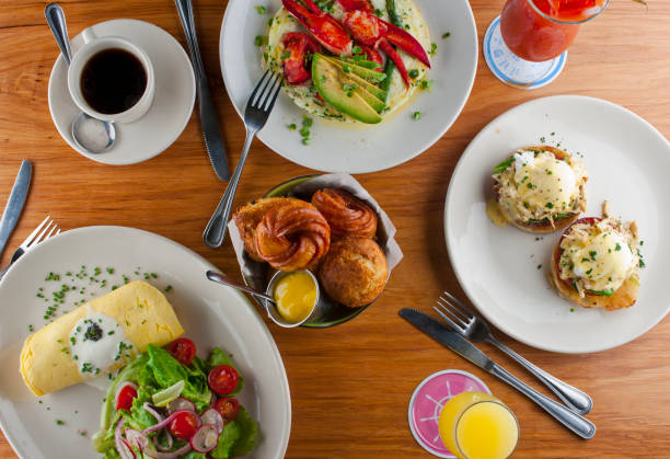 istock Breakfast or brunch table w/ food. Eggs Benedict. Eggs, Lobster, bacon, bagels, rolls, croissants, omelettes garnished w/ parsley & avocado. Classic American, French or Italian restaurant breakfast or brunch. 1253222536