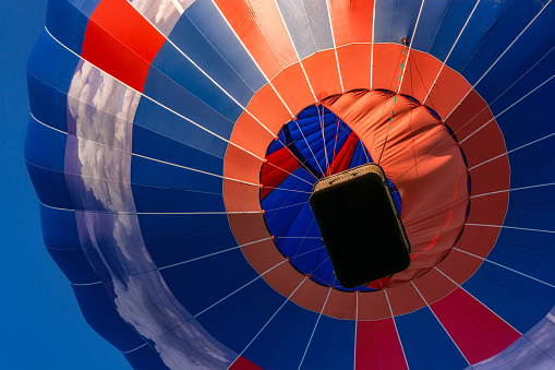 Balloon flying high in the sky. Aerostat close-up view from below. Balloon basket. Aeronautic sport. Burning gas. Bright multi-colored balloon. Romantic trip.