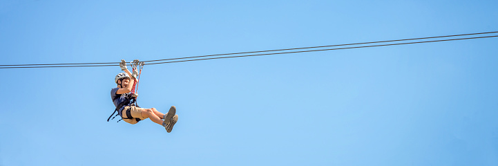 Adolescente divirtiéndose en una tirolina sobre el fondo panorámico del cielo azul con espacio de copia. photo