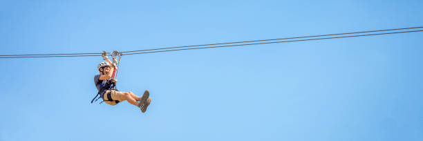 istock Teenager having fun on a zipline on panoramic blue sky background with copy space. 1253225488