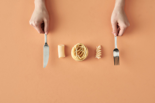 Fettuccine tortiglioni and fusilli pasta and hands with fork and knife, photography for food blog or advertising . High quality photo