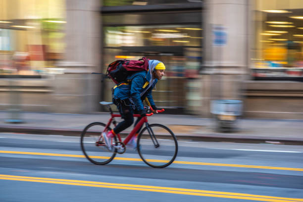 Mixed Race Bicycle Messenger Cycling on City Street Blurred motion side view of biker in early 30s wearing backpack and moving past camera on downtown street in Los Angeles. commuter photos stock pictures, royalty-free photos & images