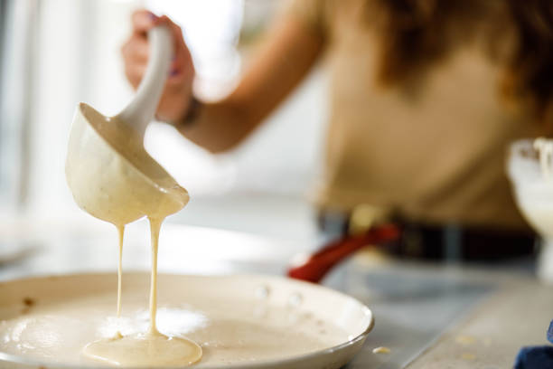 Close up of unrecognizable woman pouring dough from a ladle while preparing pancakes.