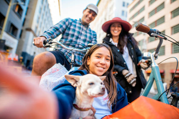 Portrait of Active Family on Bicycles in Downtown District Low angle front view of mature couple and young daughter with chihuahua enjoying sustainable lifestyle as they rides bikes in downtown open street. cargo bike photos stock pictures, royalty-free photos & images