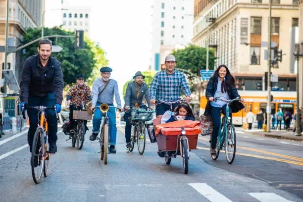 Full length front view of multi-ethnic group of adults with child and dog smiling at camera as they approach on open street in downtown Los Angeles.