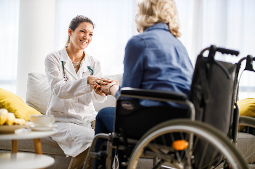 Caring female nurse communicating with mature woman in a wheelchair at nursing home.