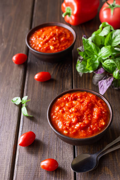 salsa balcánica ajvar en un tazón de arcilla e ingredientes para su preparación sobre un fondo de madera. comida tradicional serbia - chutney jar tomato preserved fotografías e imágenes de stock