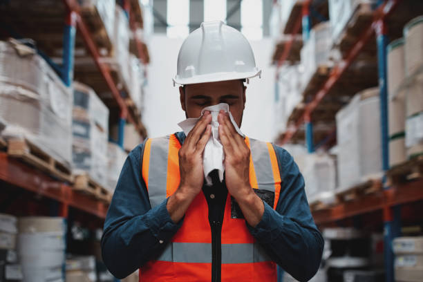 istock Warehouse manager coughing and sneezing while feeling sick and covering mouth with handkerchief 1253234327