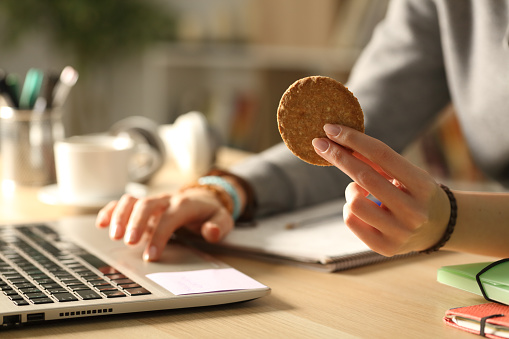 Student hands holding cookie at night studying