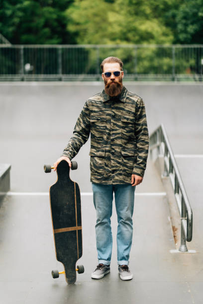 istock Bearded young man holding longboard or skateboard in the park. 1253237357