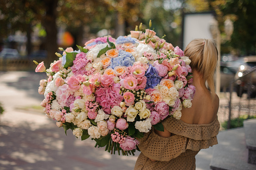 rear view of girl in beige dress who holds huge bouquet of different fresh flowers