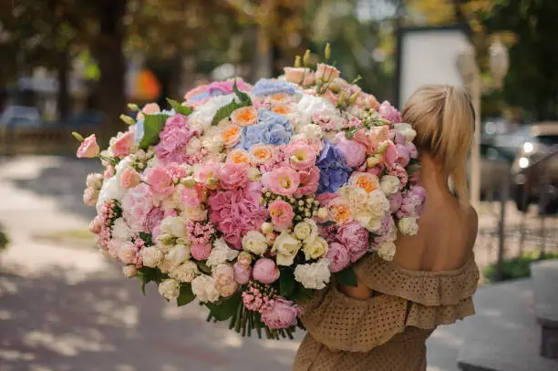 Photo of rear view of girl who holds huge bouquet of different flowers