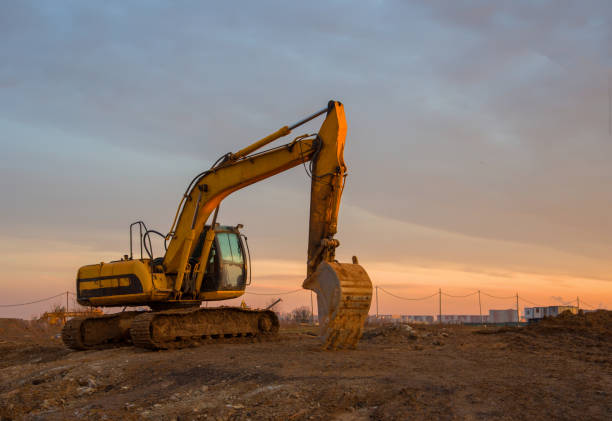 istock Excavator on earthworks at construction site on sunset background. Backhoe digs ground for the foundation and for paving out sewer line. Construction machinery for excavating 1253239540