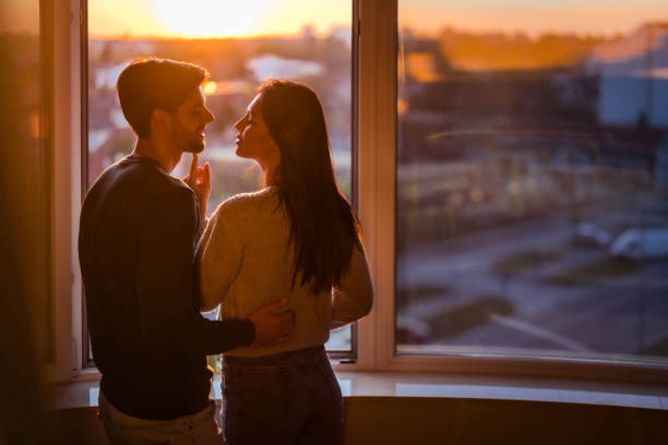 istock Back view of affectionate couple talking by the window at sunset. 1253240903