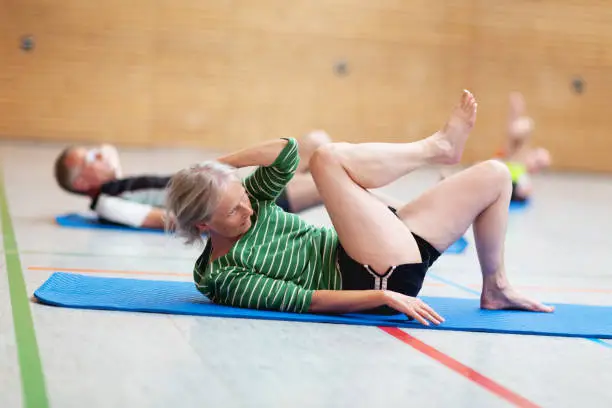 Group of adults of mixed age exercising in school gymnasium, they are doing sit-ups to strengthen abdominal muscles