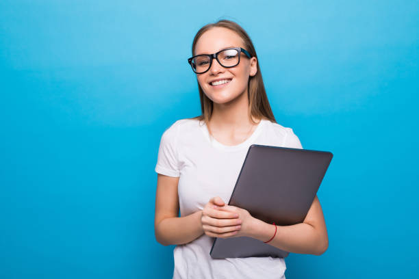 istock Young studing holding her laptop in her arms on blue background 1253246998