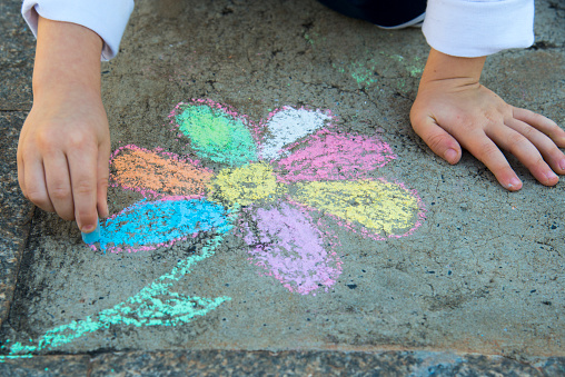 4 year old child drawing flower on sidewalk with chalk.