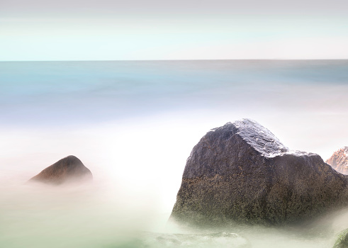 Tranquil seascape with two rocks in the smooth rolling waves like misty fog