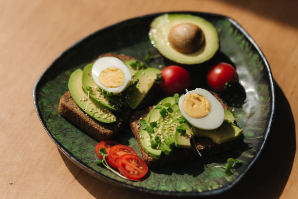 istock Delicious breakfast at home. Sandwich with fresh sliced avocado above rye bread with cherry tomatoes and boiled egg on green plate 1253248121