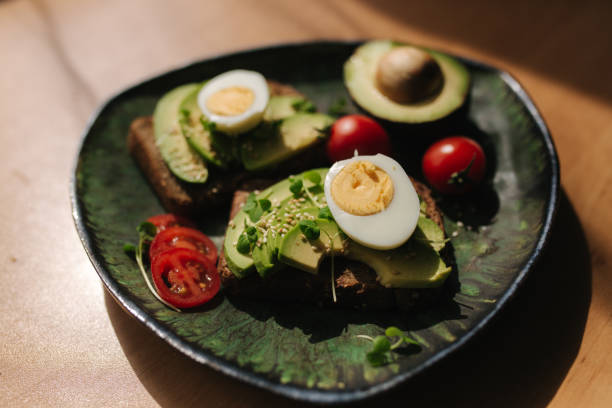 istock Delicious breakfast at home. Sandwich with fresh sliced avocado above rye bread with cherry tomatoes and boiled egg on green plate 1253248244