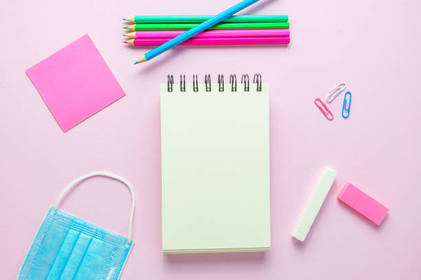 istock Blank notepad, school supplies and a blue face mask on a pink background 1253249114