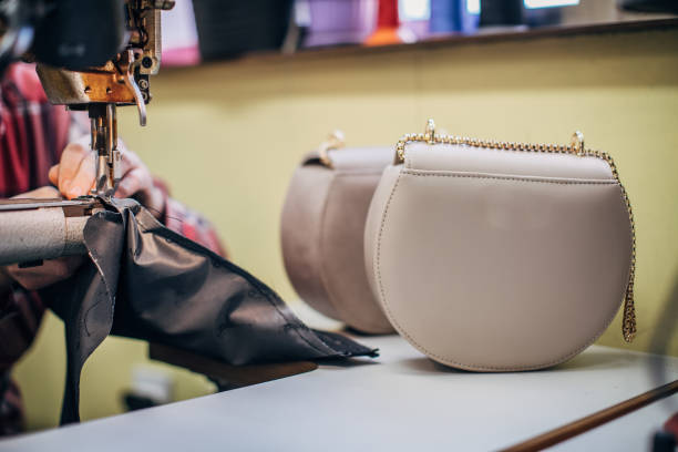 One mature man working on sewing machine in workshop, making female leather purse.