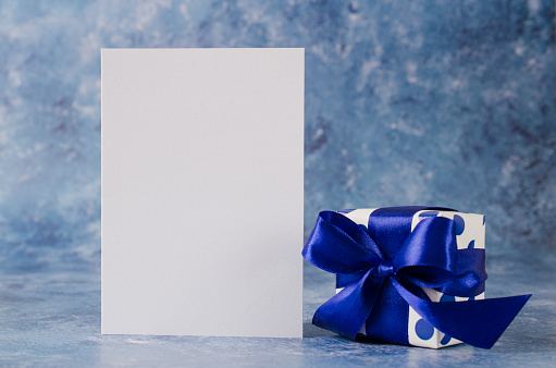 Greeting card for Father's Day or Birthday. Gift box with blank white paper on blue background. Mock up.