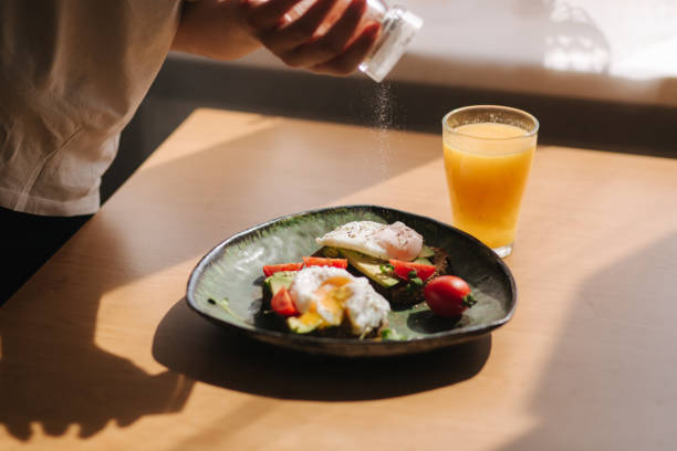 Delicious breakfast at home. Woman salt Sandwich with fresh sliced avocado above rye toasted bread with cherry tomatoes and poached egg on green plate. Fresh orange juice Yolk flows out on toast