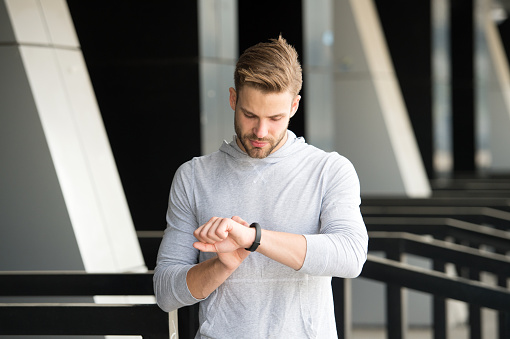 Man athlete on strict face checking fitness tracker, urban background. Athlete with bristle with fitness tracker or pedometer. Sportsman training with pedometer gadget. Sport gadget concept.