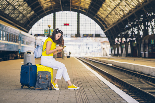 smiling pretty woman sitting on yellow suitcase with wheels at railway station travel concept