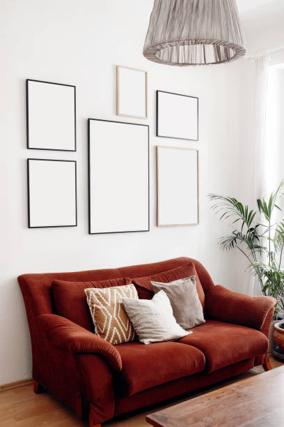 istock Blank picture frames mockups on white wall. White living room design. View of modern boho, scandi style interior with sofa, cushions, potted palm plant. Home staging concept, decorating. Vertical. 1253251668