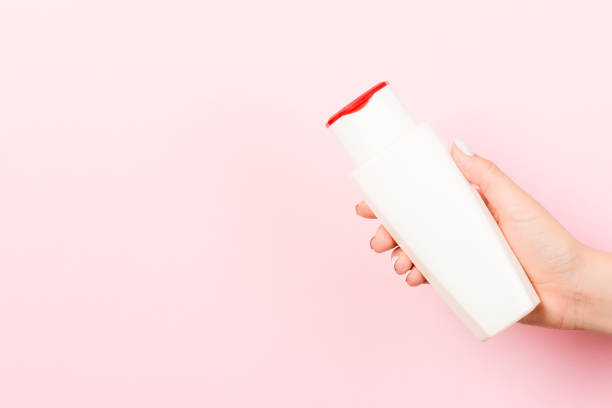 istock Female hand holding cosmetics bottle at pink background with empty space for your design 1253252059