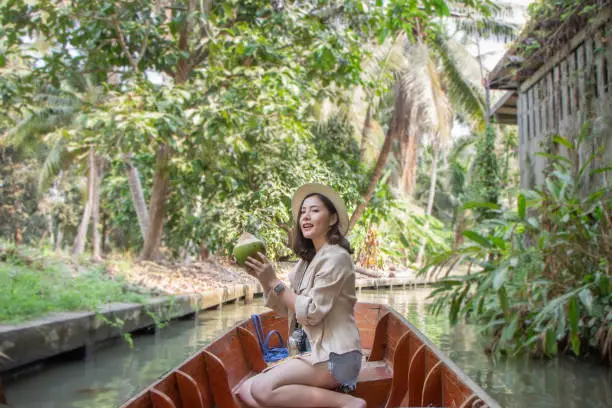 Photo of asia female tourists wearing hat holding camera and smartphone take photo vlog live . Beautiful woman take taxi boat visiting Damnoen Saduak floating market,Ratchaburi.