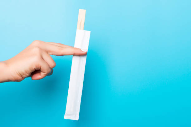 istock Female hand giving a packet with chopsticks on blue background. Sushi concept with empty space for your idea 1253253037