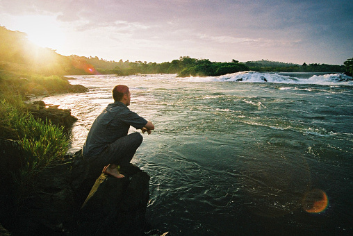 Rear side view of a young man staring at the rapids of the Nile River at the source out of Lake Victoria at Jinja Town, Uganda.