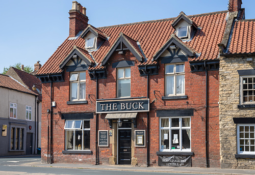 Thornton Dale, UK.  June 26, 2020.  Typical English public house. A re-brick building situated on a corner of a village street. A blue sky is above.