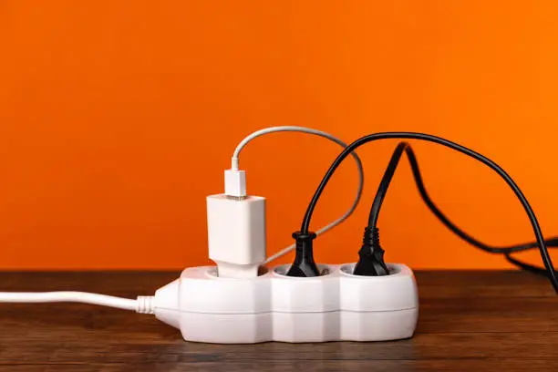 Photo of White extension cord with three plugs on orange background