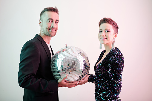 Smiling male and female singers holding disco ball and looking at camera