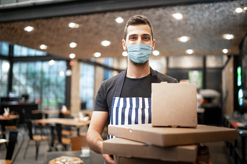 Portrait of delivery young man holding boxes at restaurant