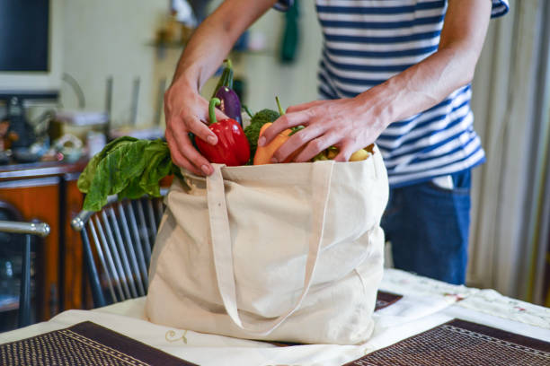 Asian man unpacking groceries at kitchen island Asian man unpacking groceries at kitchen island. He is removing fruits and vegetables from reusable bags. zero waste photos stock pictures, royalty-free photos & images