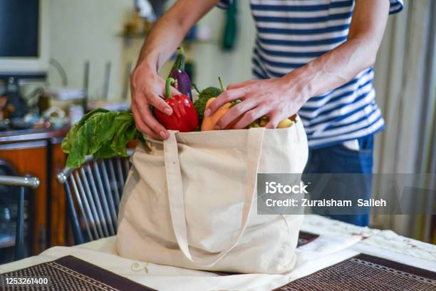 Asian Man Unpacking Groceries At Kitchen Island Stock Photo - Download Image Now - Groceries, Shopping, Reusable Bag